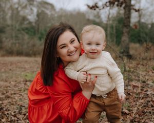 A joyful autumn family photoshoot with parent and child playing in fallen leaves while wearing red and beige outfits.