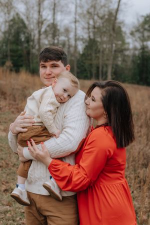 A family poses together in an outdoor autumn setting with bare trees in the background.