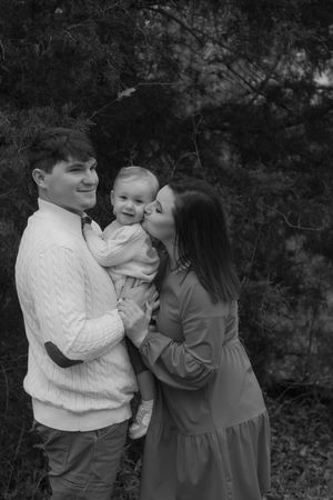 A black and white portrait of a family sharing a tender moment outdoors.