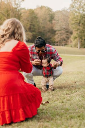 Outdoor family moment with baby taking first steps in matching plaid outfits.