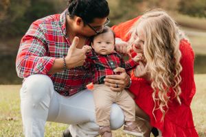 Family kneeling together on grass sharing intimate moment with baby in coordinated outfits.