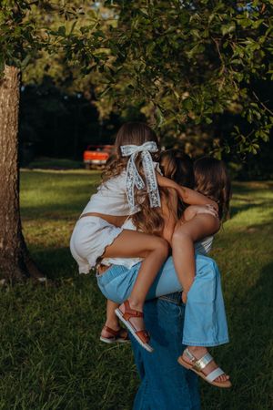 A tender outdoor moment captured in warm sunlight under a tree, with matching white and silver sandals.