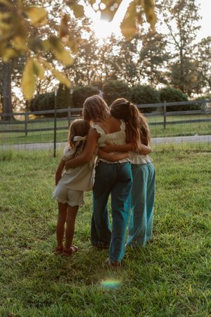 A group embraces in a sun-drenched field at sunset with a wooden fence in the background.