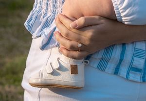 Close-up of hands holding baby's foot wearing white shoes.