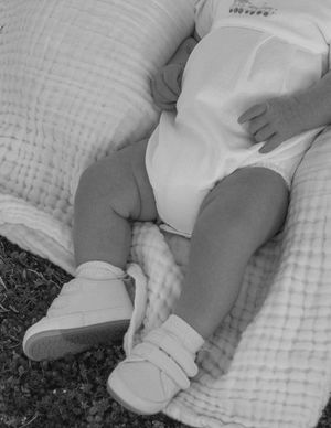 Black and white image of baby's legs in white shoes on quilted blanket.