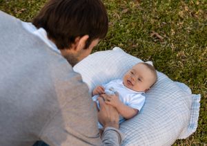 Baby in light blue outfit lying on quilted blanket while caregiver leans in.