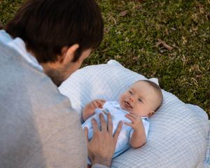 A newborn baby lying on a white blanket outdoors while being gently touched by an adult in gray.
