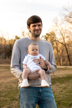 Parent and baby share a tender outdoor moment during sunset photo session.