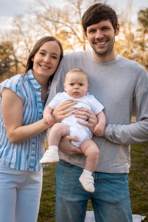 Family of three poses together outdoors during golden hour photo session.