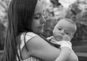 Black and white portrait of parent and baby in intimate embrace outdoors.
