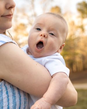 Joyful baby in white onesie laughing while being held outdoors.