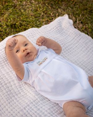 A baby in a light blue outfit lying on a white textured blanket outdoors.