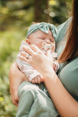 Sleeping baby in mint green outfit with matching headband being cradled outdoors.