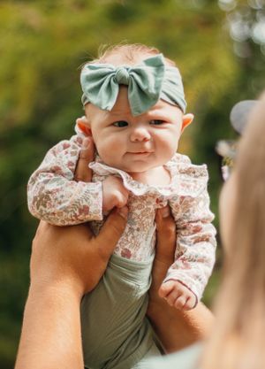 Close up of a smiling baby wearing a mint bow headband and floral print outfit.