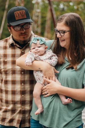 Casual outdoor family portrait with baby wearing mint bow and parents in relaxed attire.