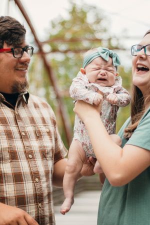 Parents laughing with their baby who is wearing a mint headband and floral outfit.