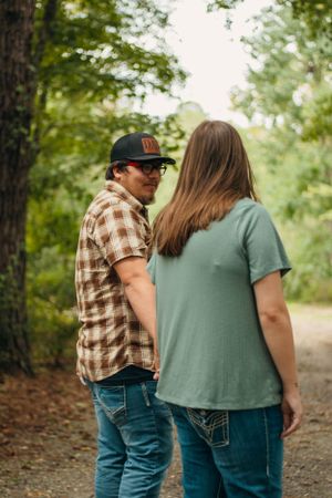 Couple in casual wear standing together on a wooded path.