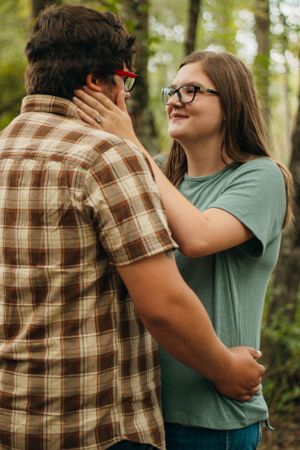 Intimate moment between a couple wearing casual attire in a forest setting.