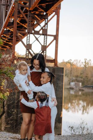 Family members share joyful moments together while posing near a rustic bridge at sunset.