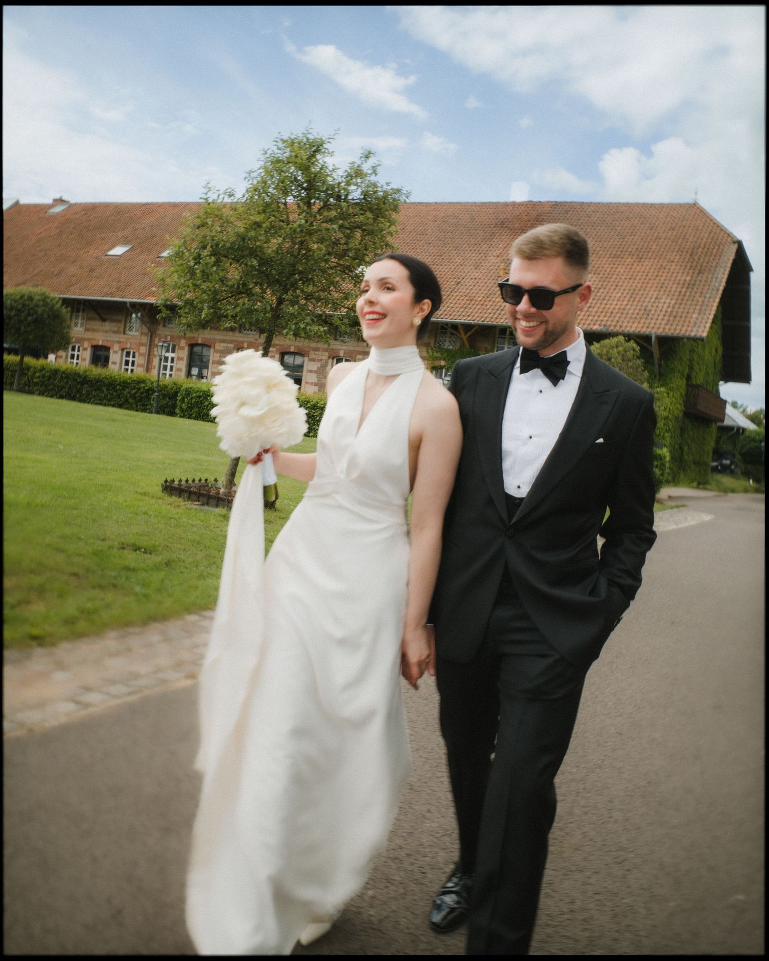 Wedding couple walking along a path near brick buildings on sunny day.
