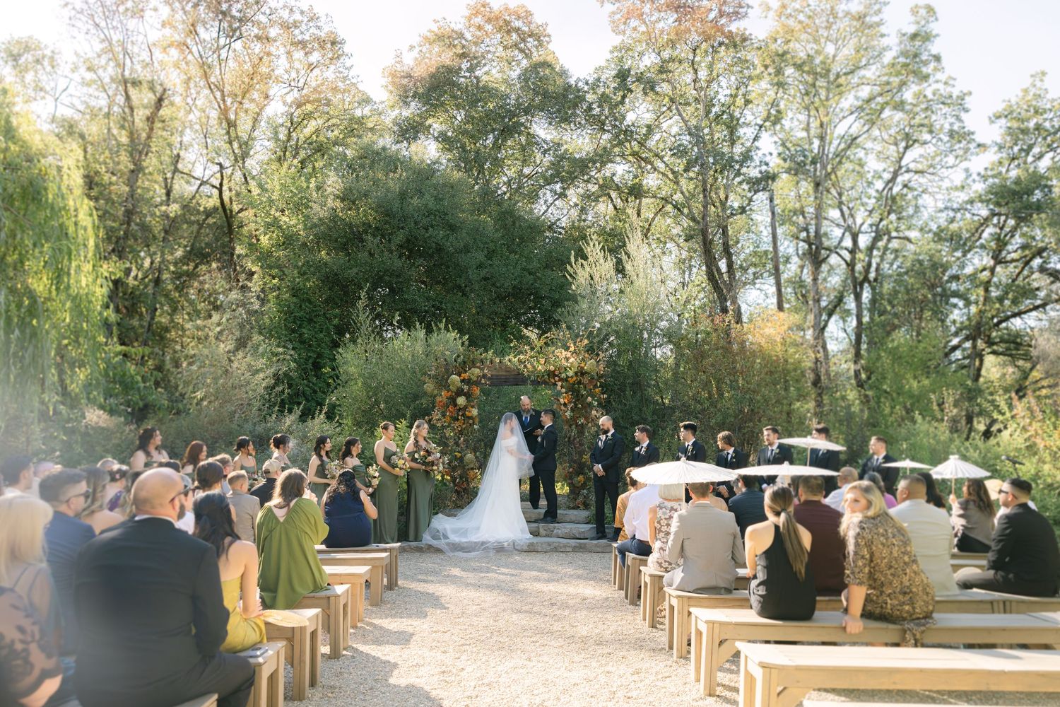 Outdoor garden wedding ceremony with guests seated on wooden chairs along a gravel path.