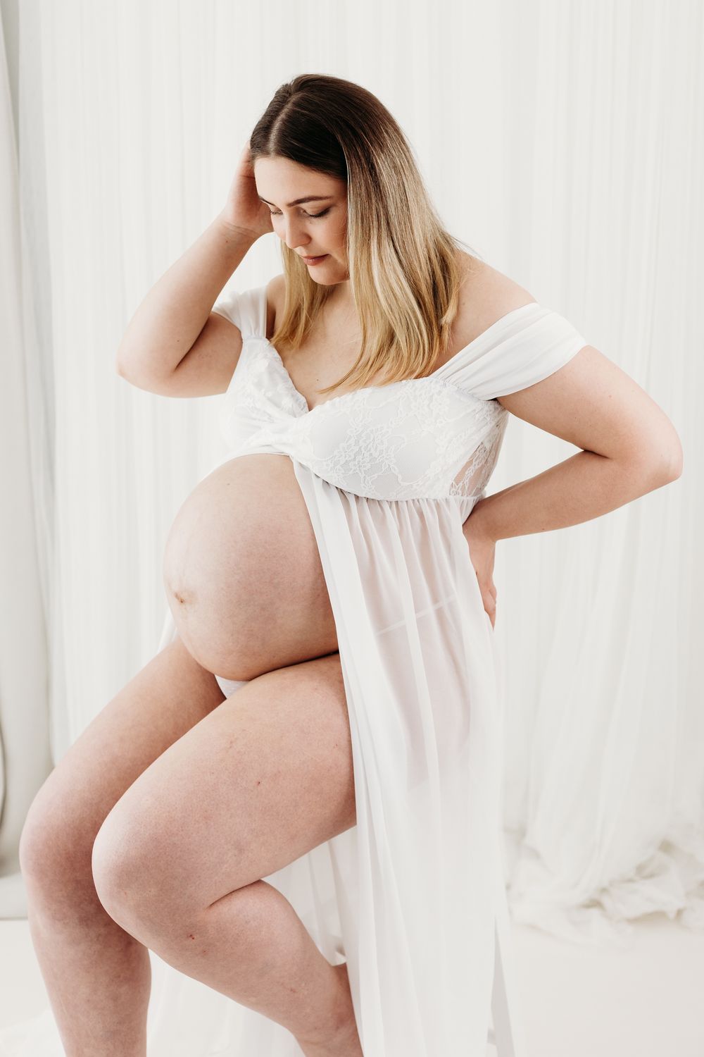 Elegant maternity portraits in Nottingham studio, glowing expectant mum captured with natural light and minimal styling looking down at bump
