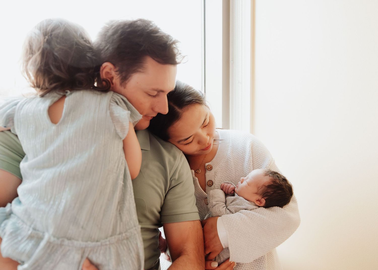Tender family moment as parents cuddle with their newborn baby by a bright window.