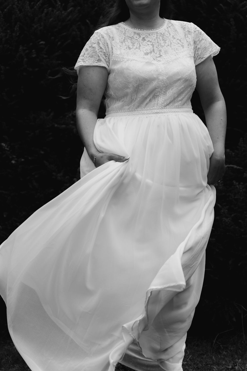 A close-up black and white photo of a wedding dress with lace bodice and flowing tulle skirt.