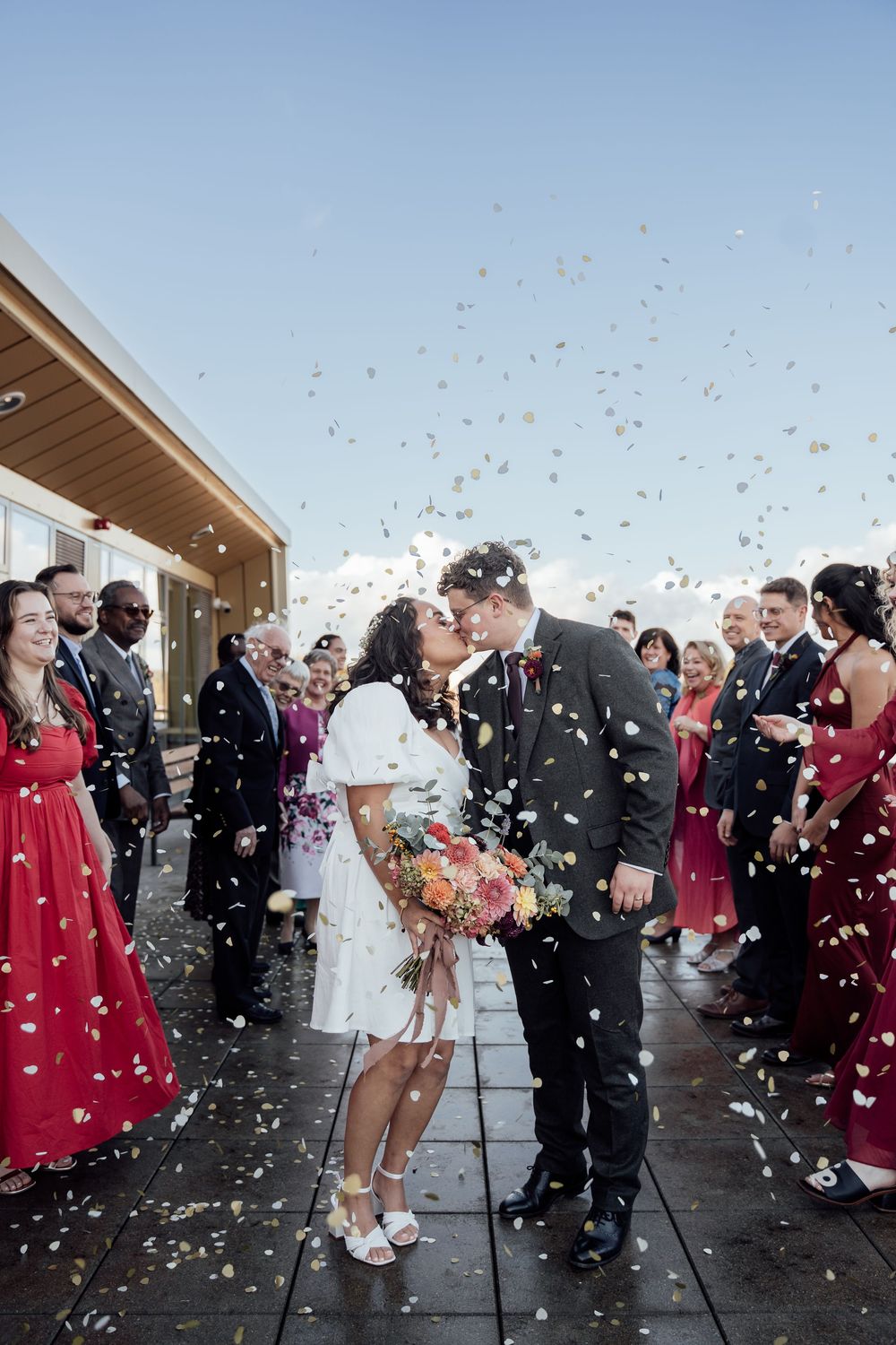 Wedding guests throw confetti over the newlyweds during an outdoor ceremony exit celebration.
