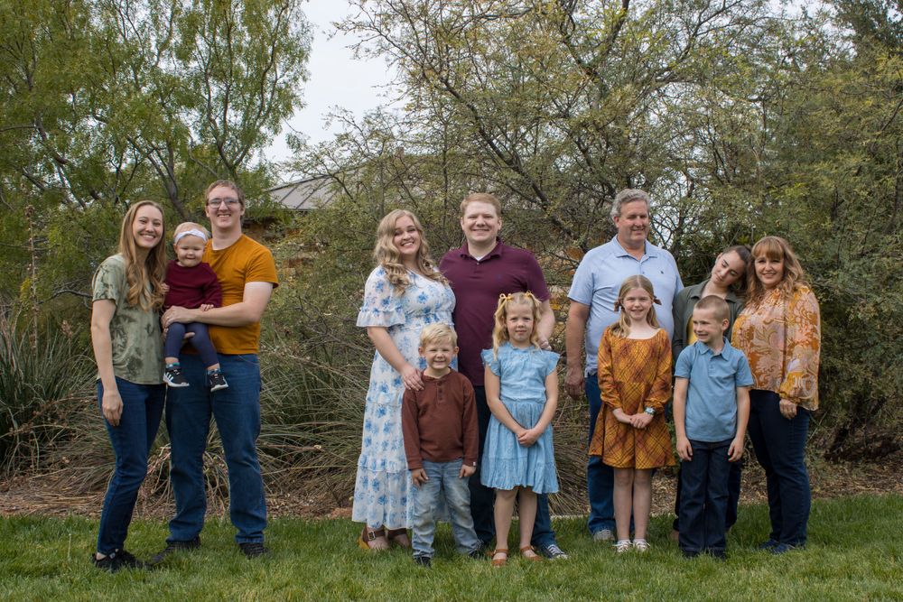 An extended family group of ten smiles together on a green lawn with lush trees in the background.