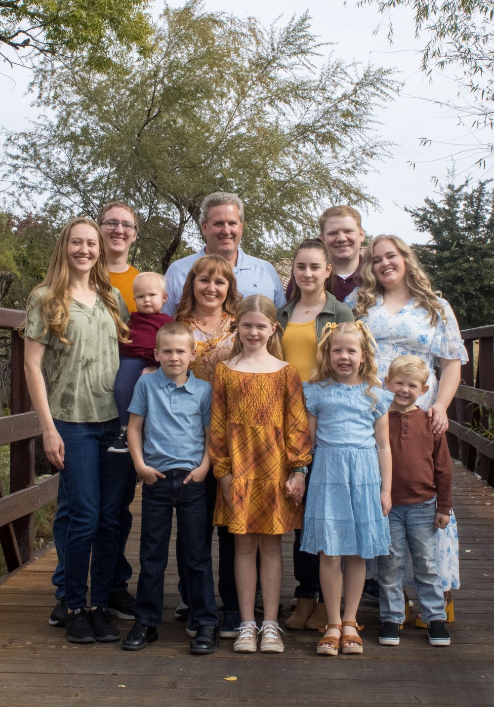 Large extended family of eleven posing together on a wooden bridge in autumn.