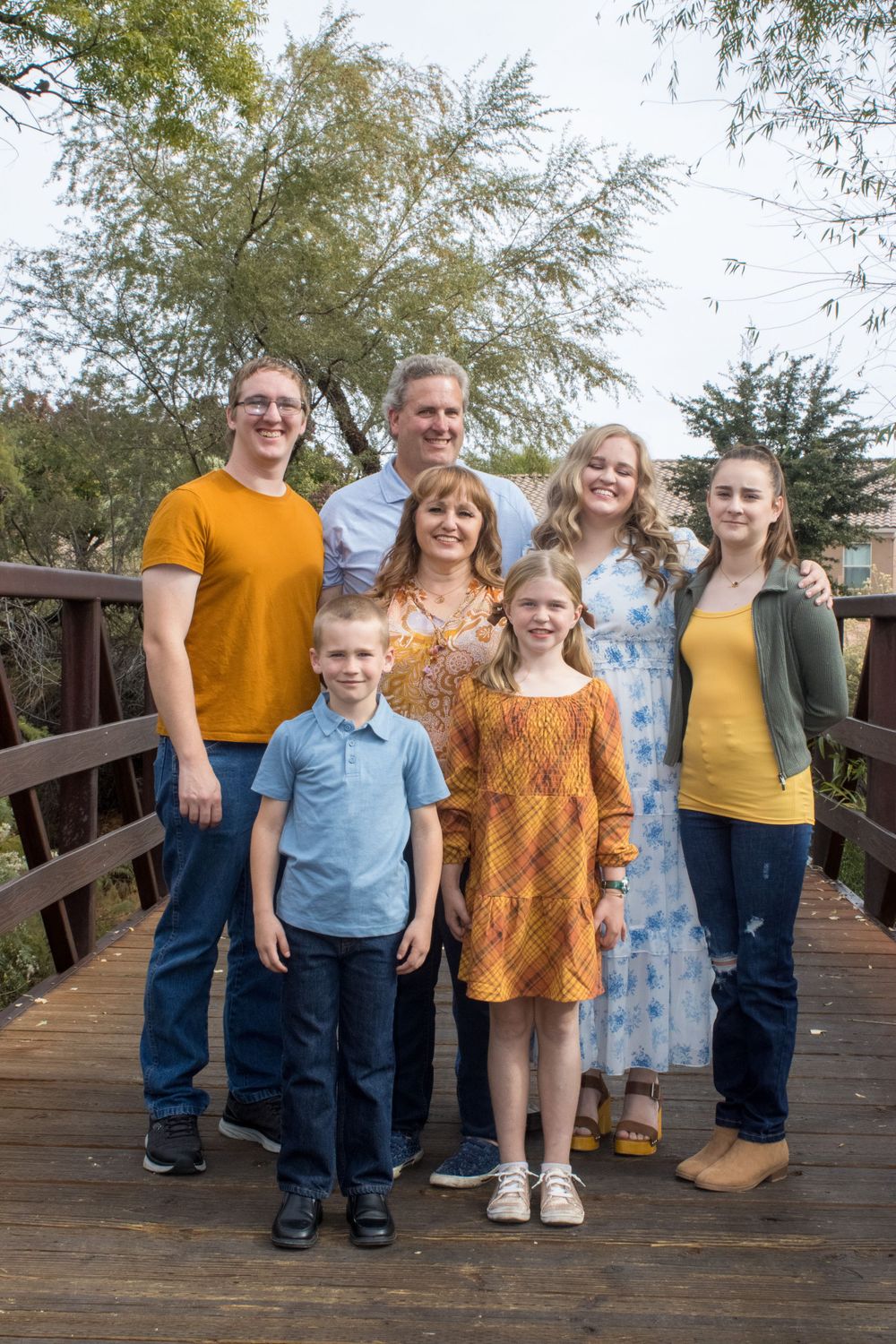 Extended family of seven poses together on a wooden bridge for an outdoor portrait.