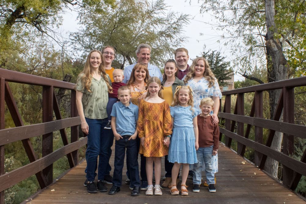 Large extended family poses together on a wooden bridge surrounded by autumn trees.