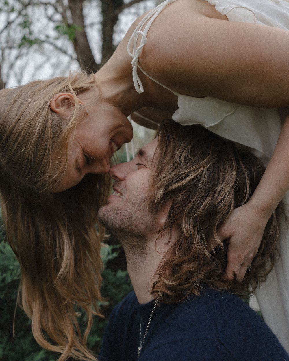 A romantic couple sharing a tender kiss outdoors, with the woman leaning down toward the man amidst lush greenery.