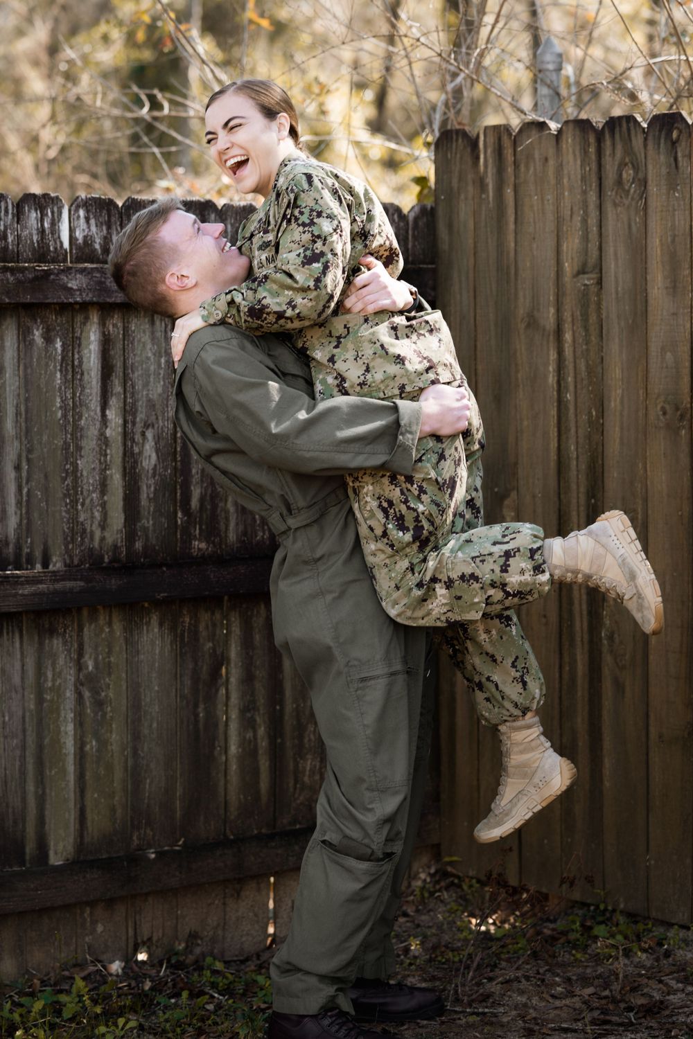 A military service member in uniform lifts up another service member in a joyful embrace.