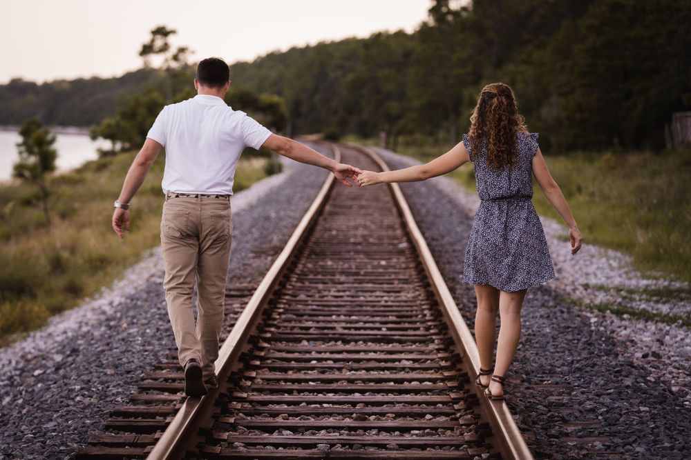 A couple balances on railroad tracks while holding hands at dusk.