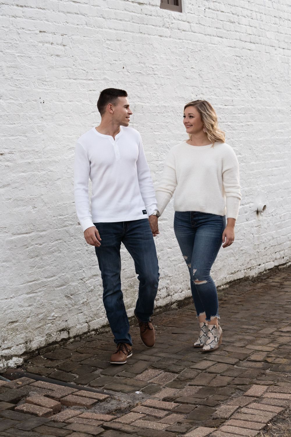 Couple in matching white sweaters walking on cobblestone path.