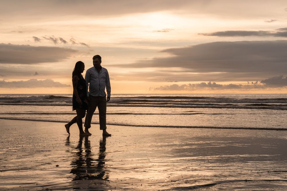 A silhouetted couple stands together on a beach at sunset.