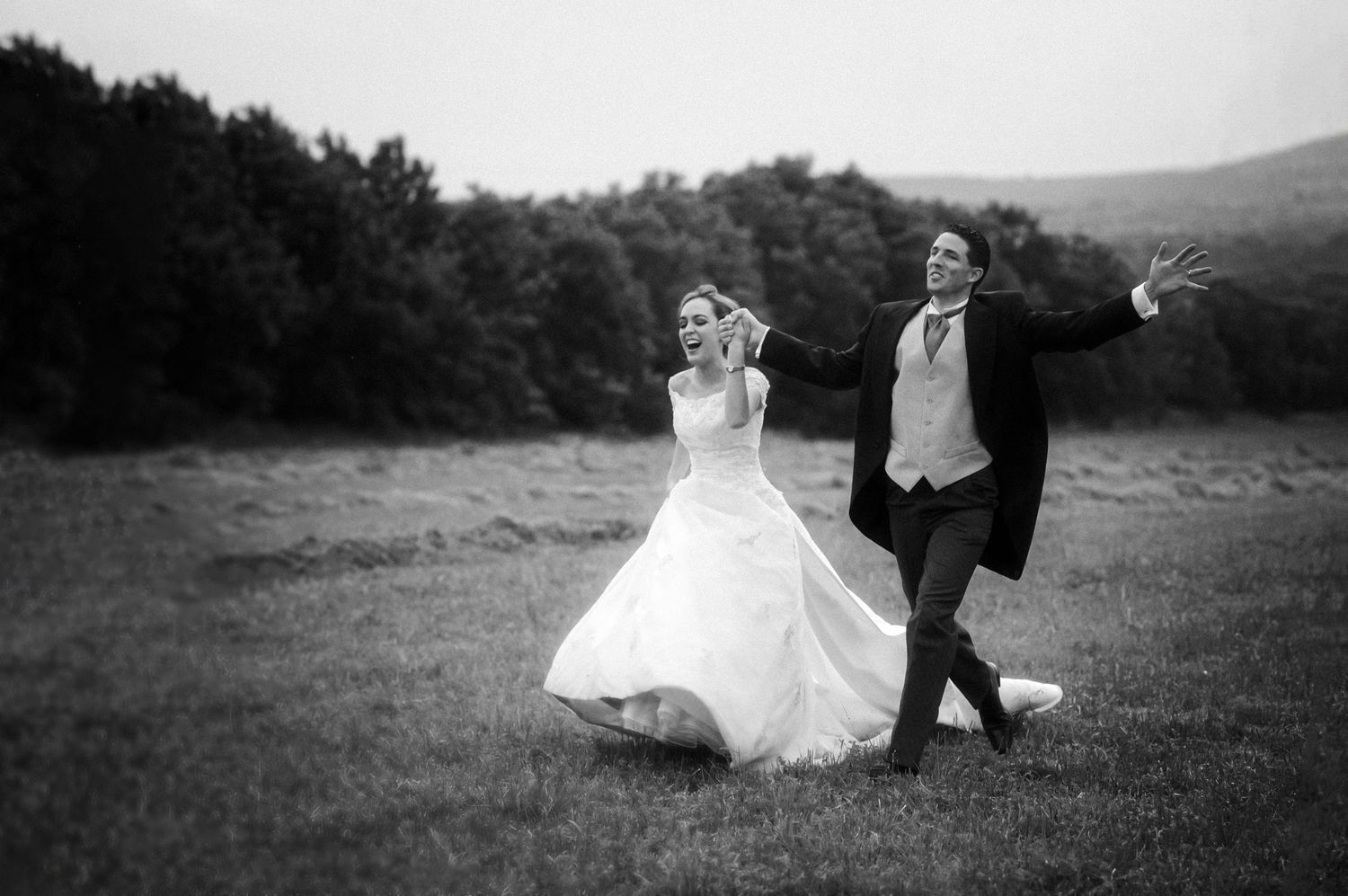 A playful black and white portrait of a couple walking together in a meadow.