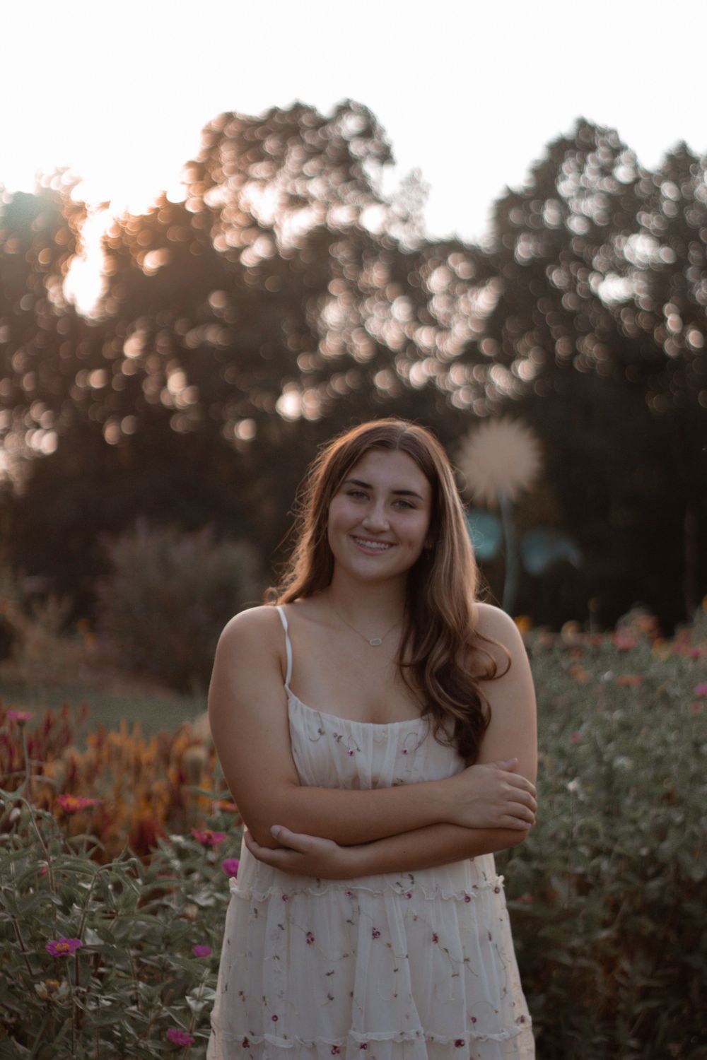 A backlit portrait in a floral dress surrounded by late summer wildflowers and warm sunset light.