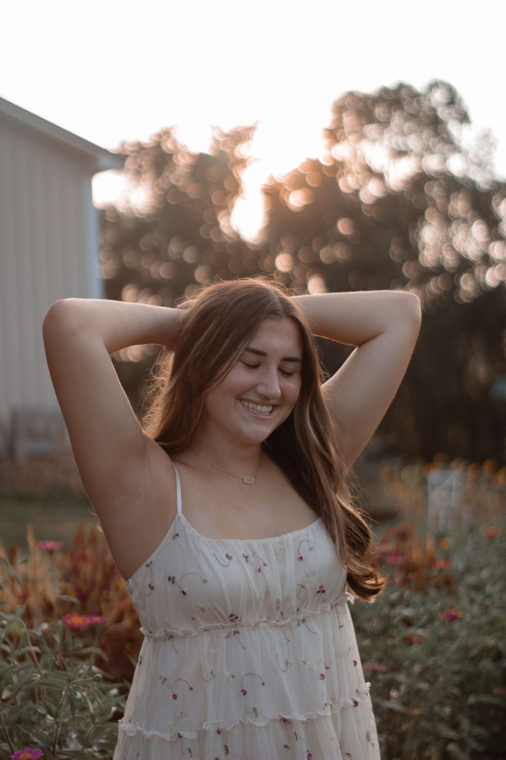 A figure in a white dress stands in golden sunlight with arms raised against a bokeh background.