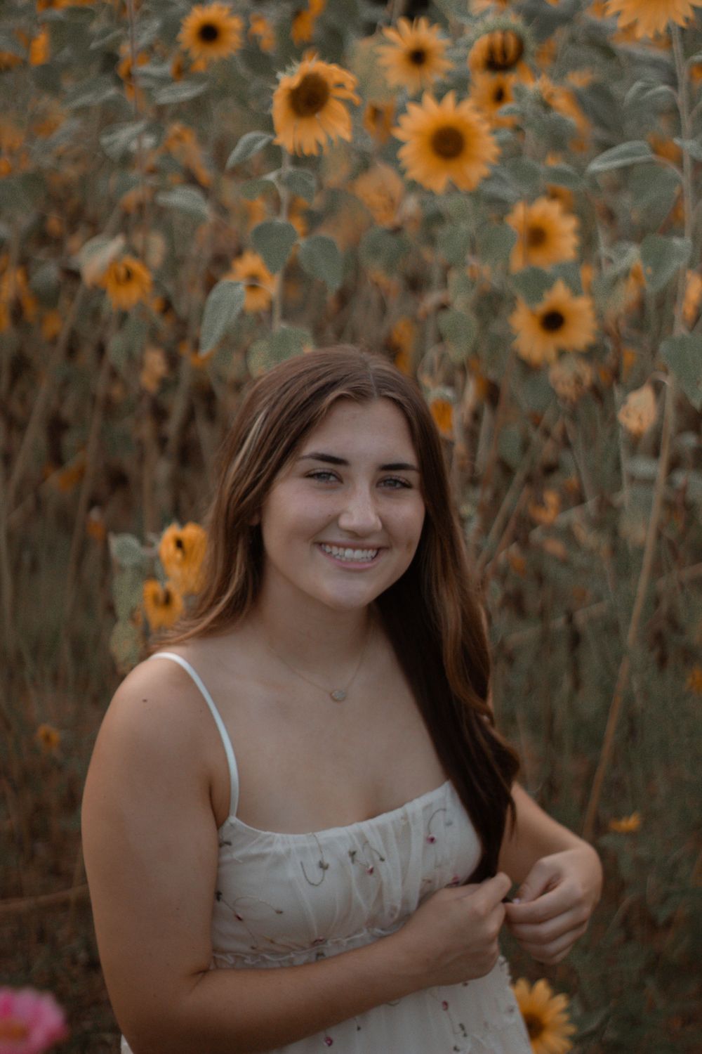 A summery portrait in a white dress against vibrant blooming sunflowers at golden hour.