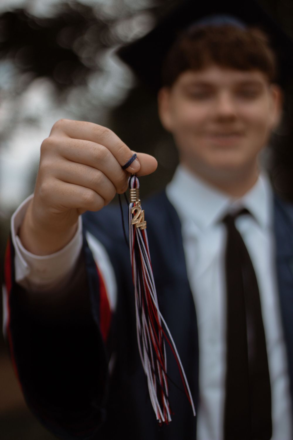 Graduate holds up a colorful graduation tassel against a blurred background.