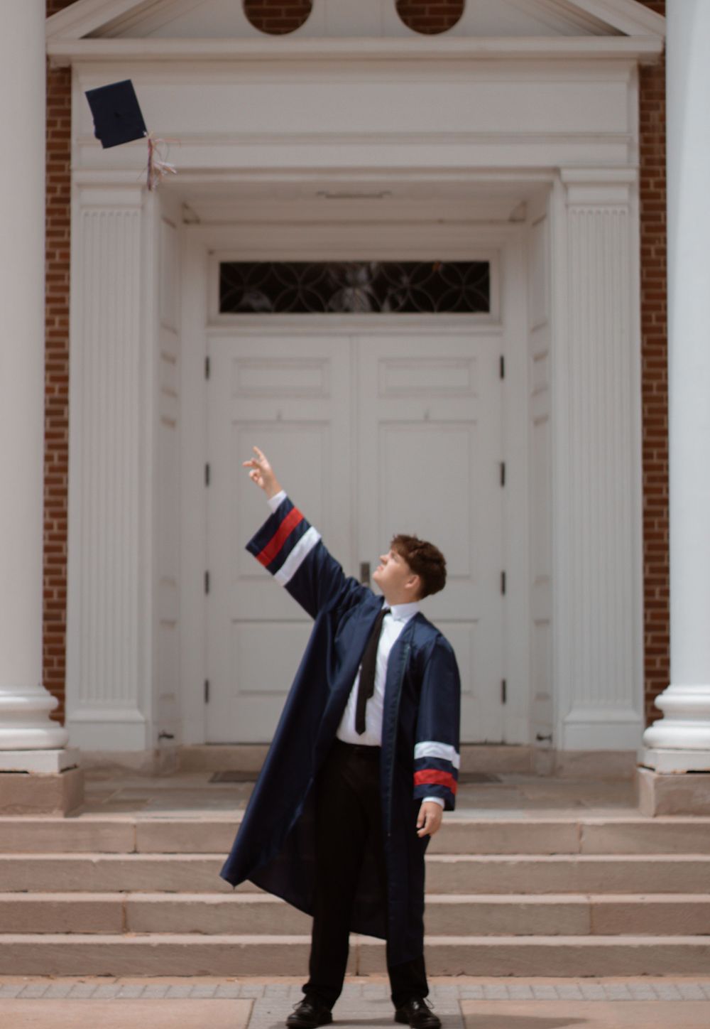 Graduate throws cap in celebration in front of white university doors.