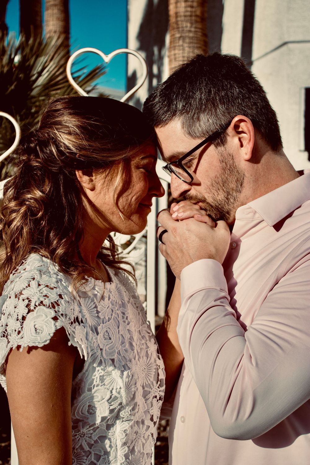 Groom kissing bride's hands tenderly during romantic Las Vegas wedding ceremony outdoors with heart decorations.