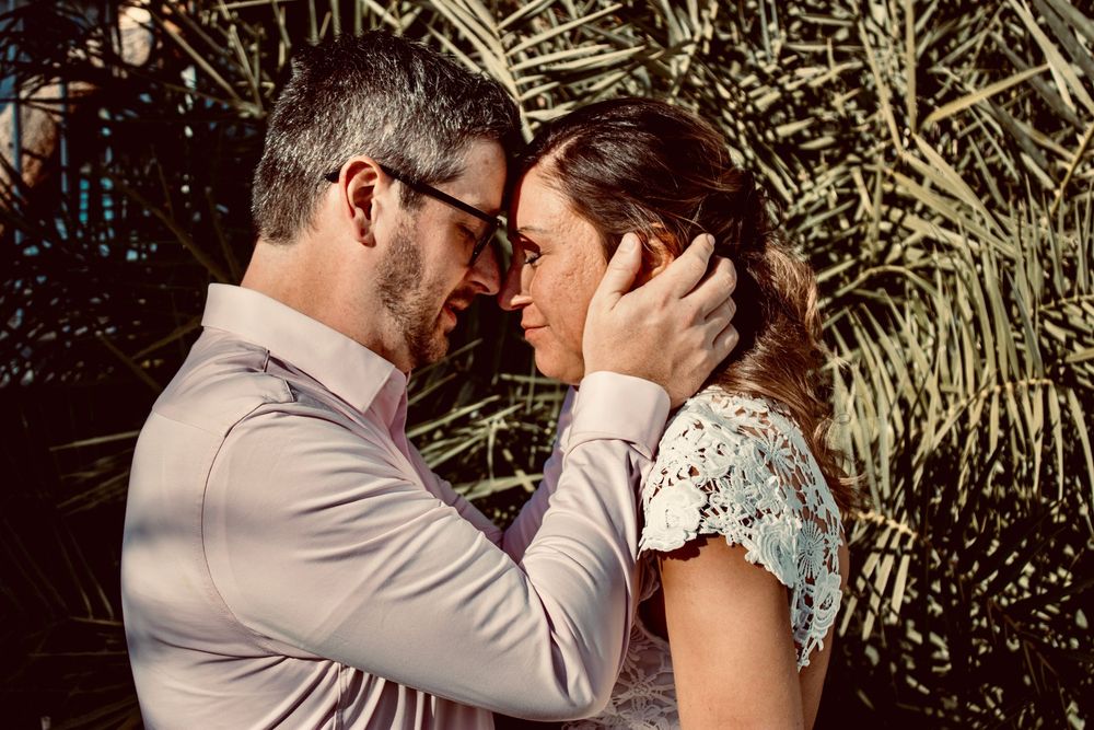 Romantic couple sharing an intimate moment, man tenderly holding woman's face near tropical palm leaves.