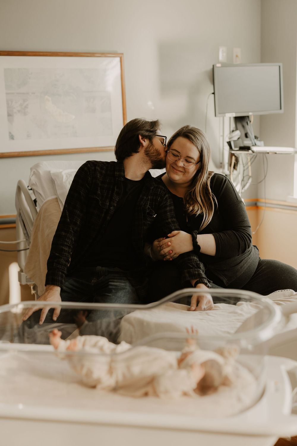 Intimate hospital room moment with couple leaning close together near medical equipment.