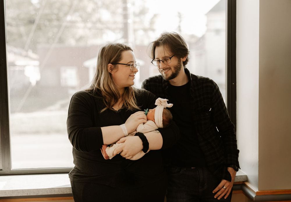 Couple sharing tender moments in black clothing near hospital window.