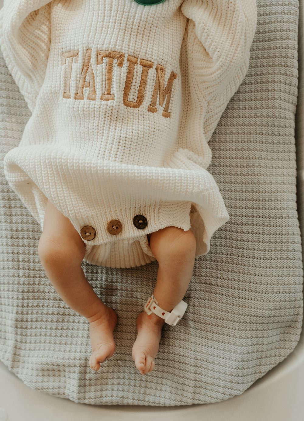 Tiny baby feet in white knitted clothing on gray blanket.