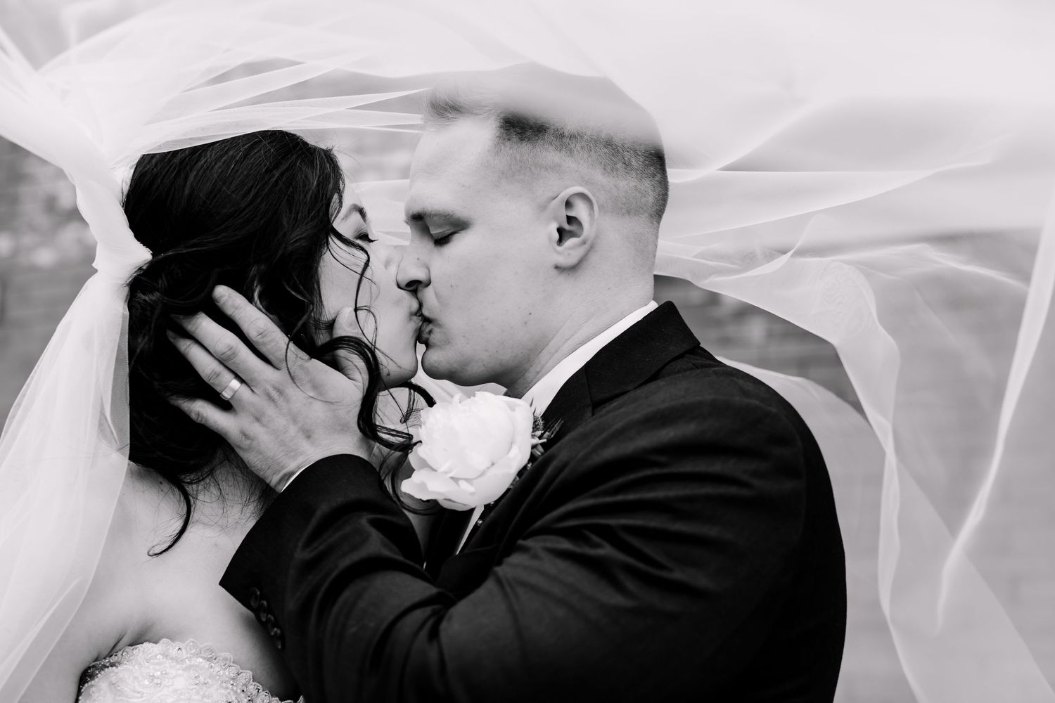 Black and white wedding portrait with bride and groom under flowing veil.